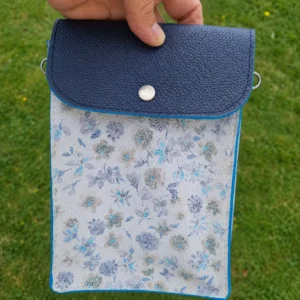 Pochette en cuir pratique chic printanière, de couleur bleu marine et blanche avec des motifs à fleurs bleues. Pour téléphone, lunettes et portefeuille. Portée en bandoulière.