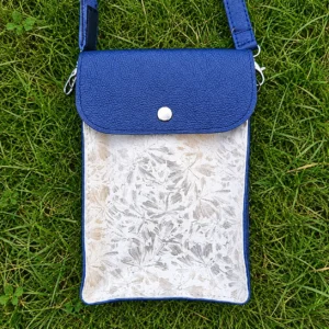 Pochette artisanale en cuir bleu marine et blanc à motifs fleuris colorés, portée en bandoulière.