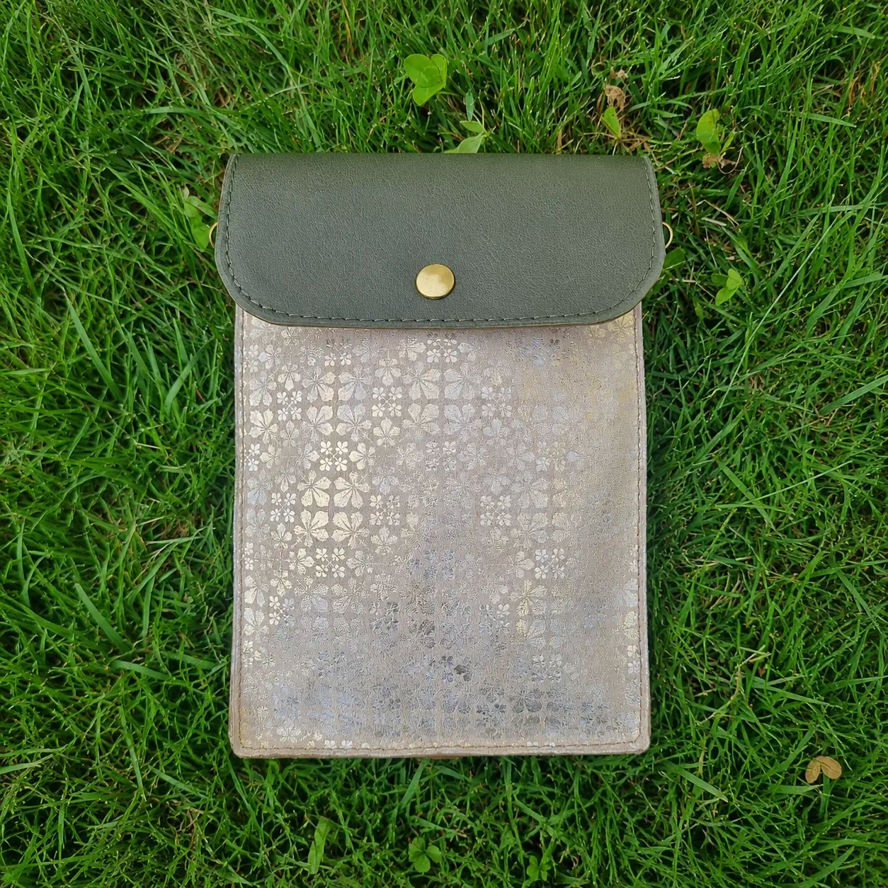 Pochette artisanale en cuir vert kaki et beige à motifs fleuris dorés, portée en bandoulière.