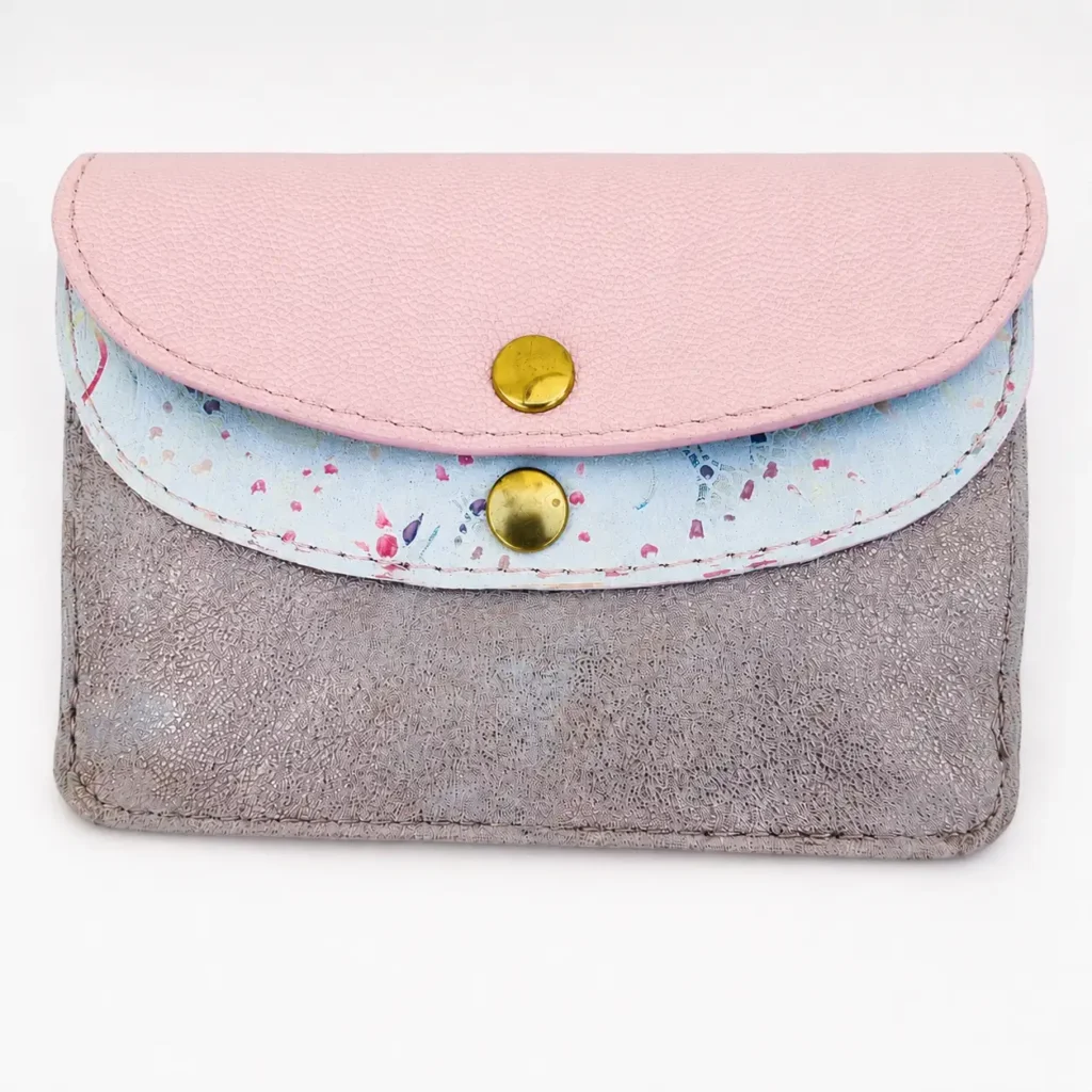 Portefeuille femme en cuir à rabats, format moyen, vue de face. Trois cuirs différents : rose pâle, blanc à motifs floraux pastel et rose poudré pailleté. (Face)