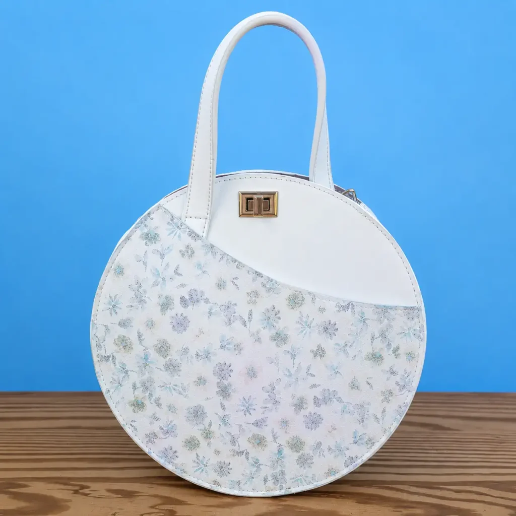 Sac rond femme en cuir blanc et cuir imprimé fleuri pastel bleu-gris, vue de face.