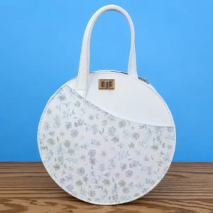 Sac rond femme en cuir blanc et cuir imprimé fleuri pastel bleu-gris, vue de face.